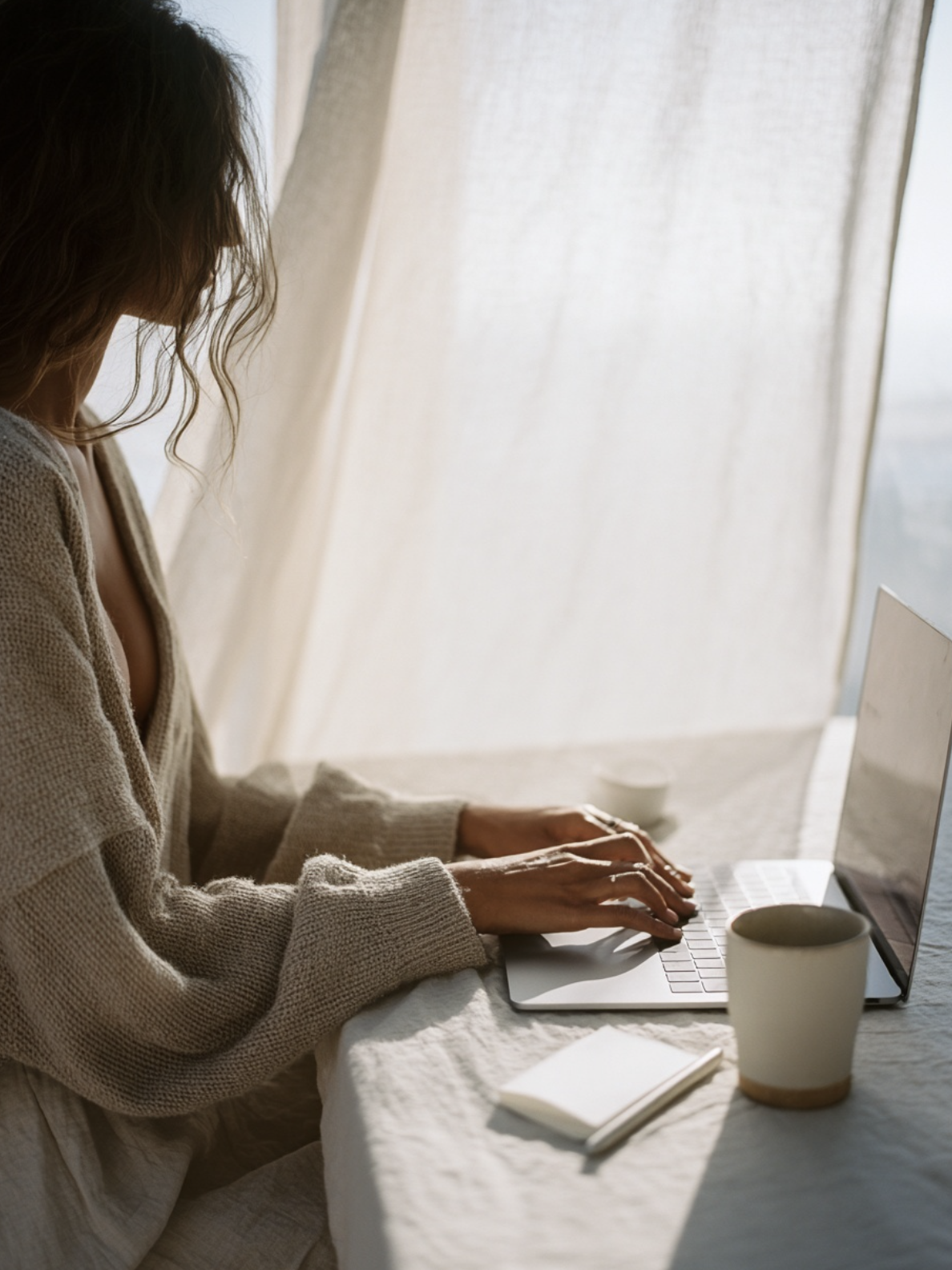 Person working on a laptop at a sunlit table with coffee and notebook, representing focused and intentional business work