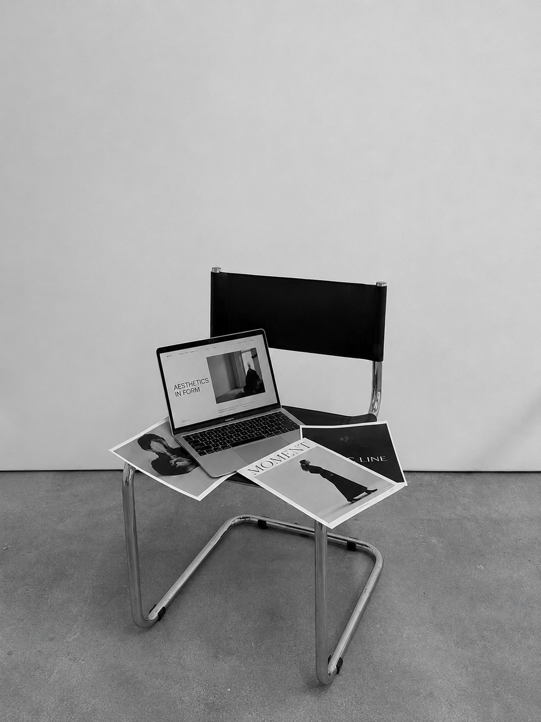 Minimal black and white workspace setup with a laptop, chair, and branding materials for a website design project